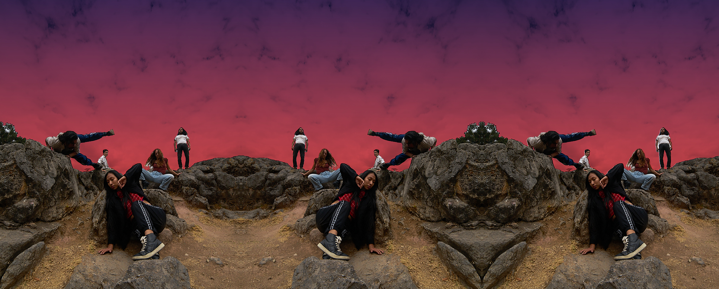 La imagen es una fotografía de varios bailarines y bailarinas que danzan sobre un terreno rocoso y arenoso. Al fondo se ve el cielo rojizo a la hora de la caída del sol.