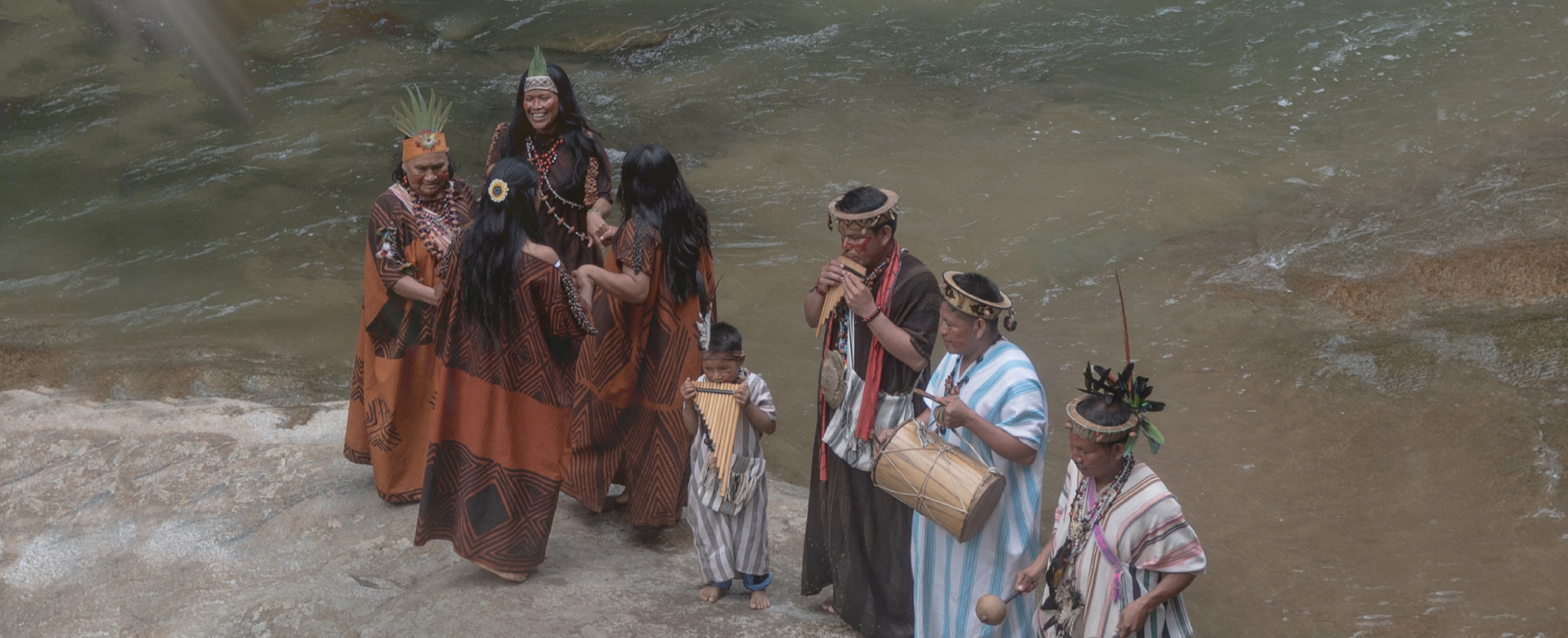 Foto que muestra, a la orilla de un río caudaloso, a un grupo de mujeres, hombres y un niño, ataviados con ropas y adornos propios de etnias ...