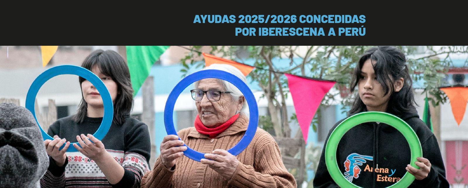 Foto que muestra a dos chicas jóvenes y una abuela que sostienen en sus manos un aro cada una frente a sus rostros. En el fondo de la imagen se ven árboles y una cadeneta de triángulos de papel de difrentes colores. En la parte superior de la imagen se lee AYUDAS 2025/ 2026 CONCEDIDAS POR IBERESCENA A PERÚ.