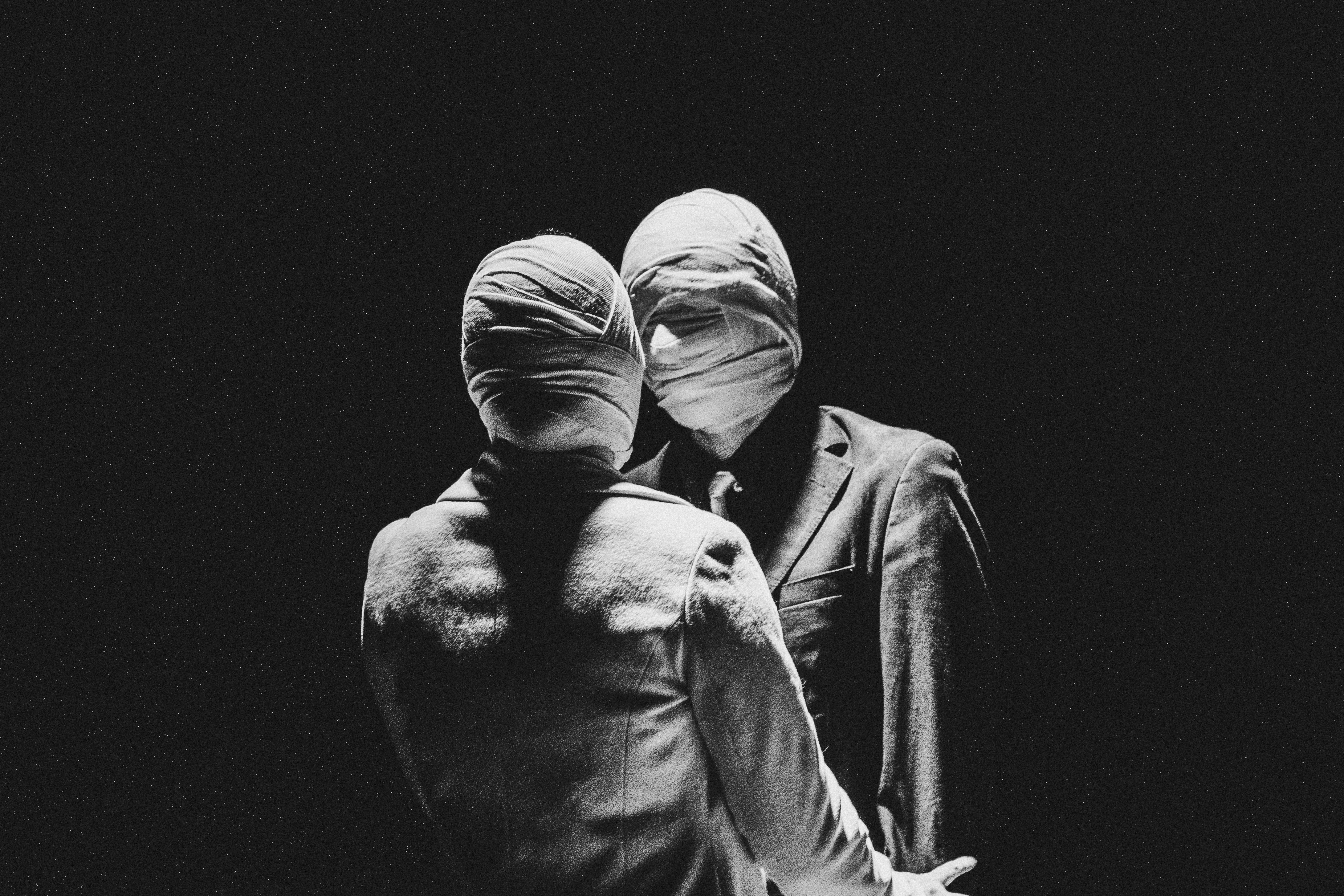 Foto en blanco y negro de dos personas paradas una frente a otra, vestidas con ternos elegantes y con las caras envueltas en bandas de gasa.