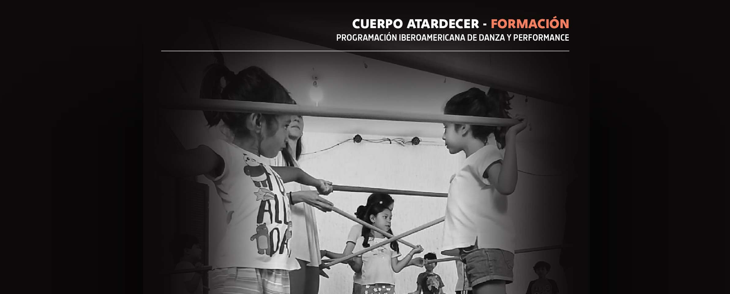 Foto de niñas y niños en salón, jugando y moviéndose con una varas que unen a los niños entre sí. En la parte superior de la imagen se lee CUERPO ATARDECER - FORMACIÓN PROGRAMACIÓN IBEROAMERICANA DE DANZA Y PERFFORMANCE.