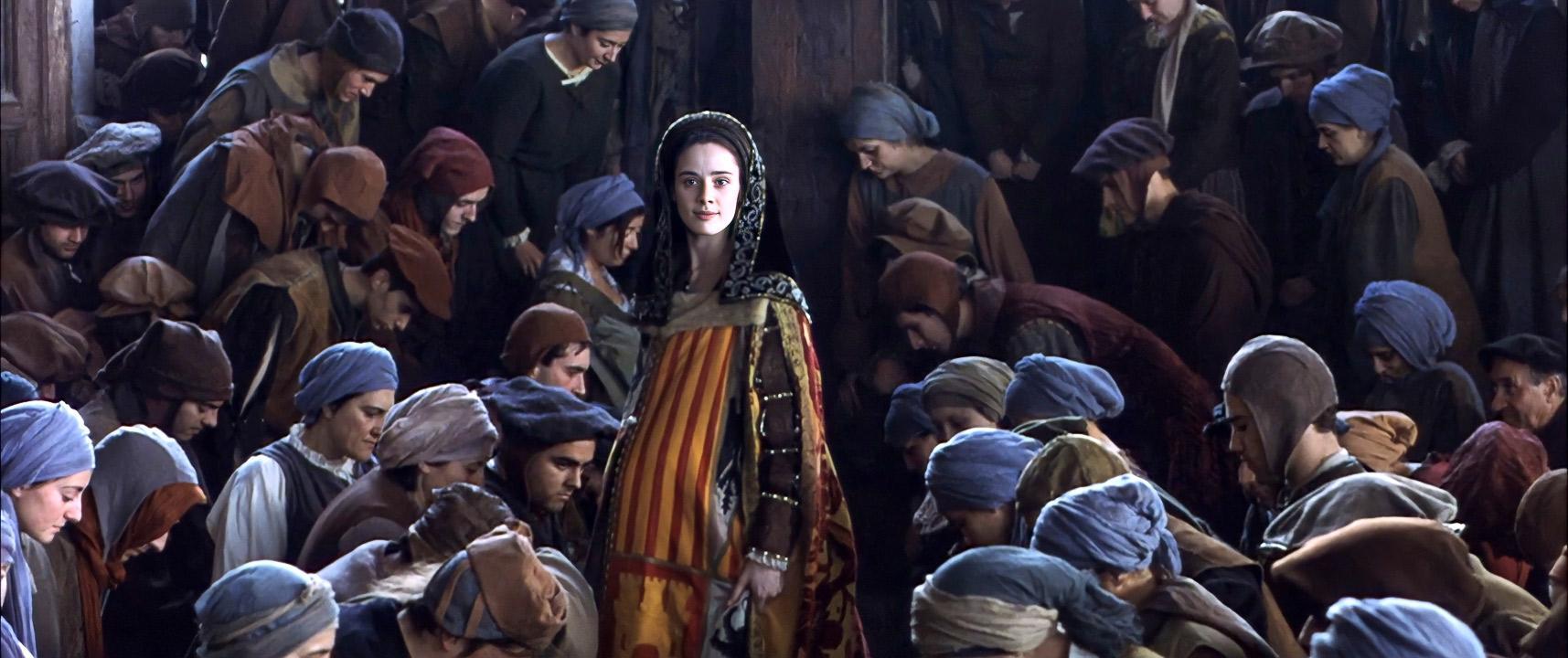Foto de una escena medieval que muestra a una joven embarazada, vestida con ropa de reina, que está parada en medio de una multitud de personas pobres que se inclinan ante ella.